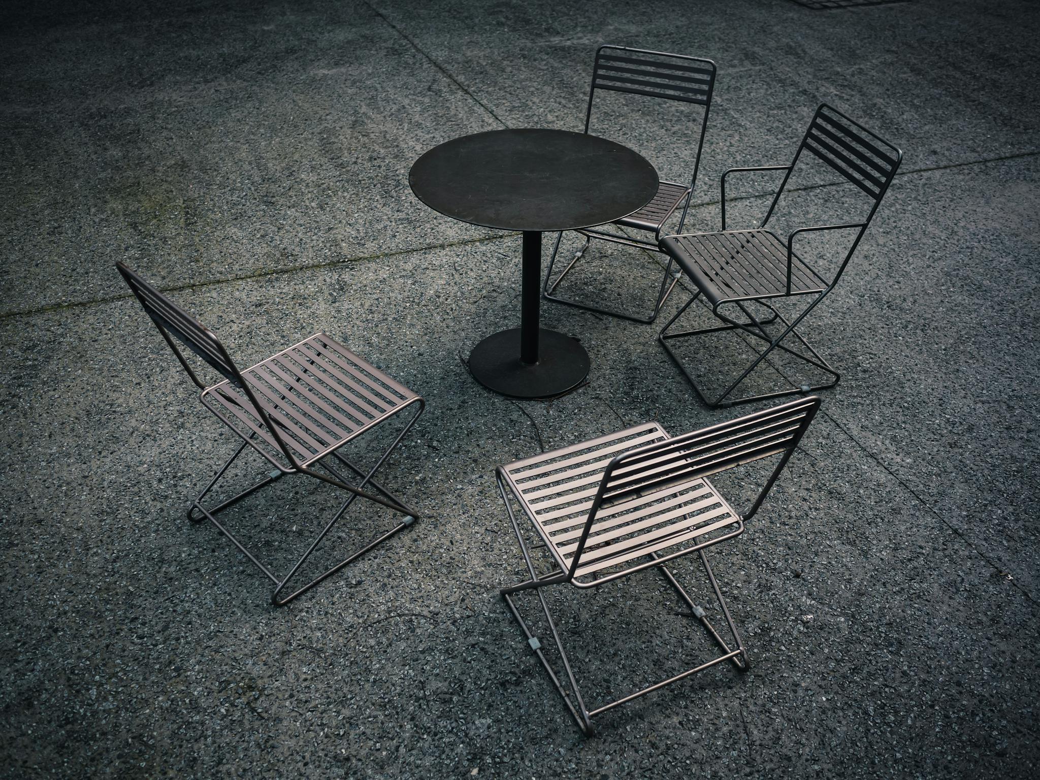 A minimalist outdoor seating arrangement with a metal table and four chairs on a textured surface.