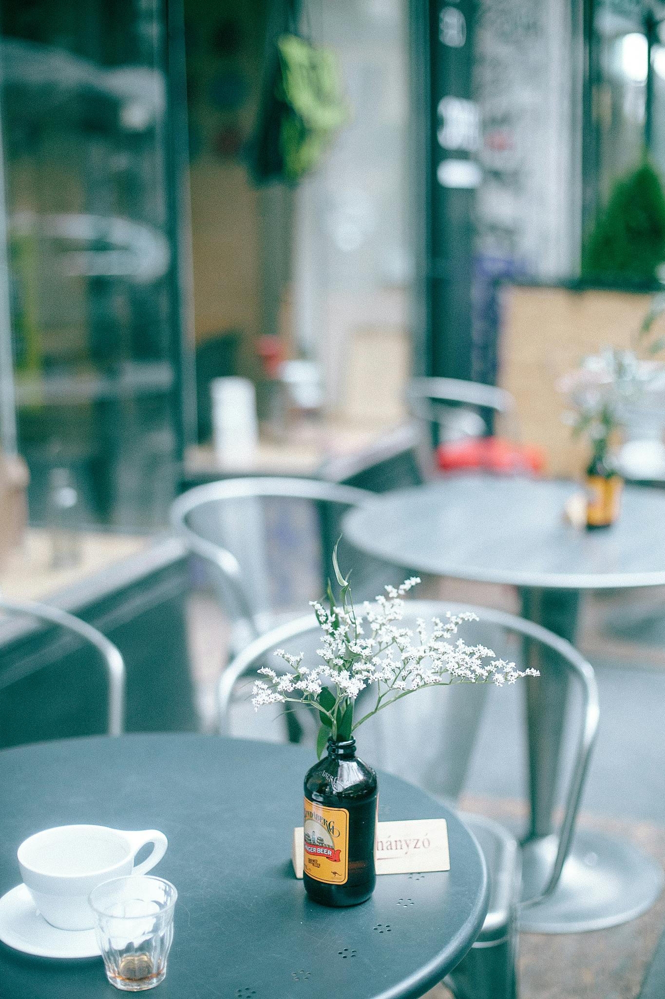 Table decorated with glass vase with fresh flowers and cup of drink located in outside cafeteria in daytime